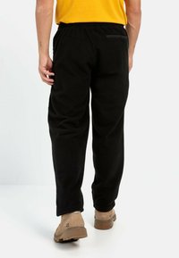 Sorte sweatpants med en afslappet pasform, elastisk talje og en baglomme, lavet af blødt stof, vist fra bagsiden.