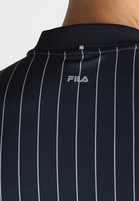 Chemise bleu marine à rayures verticales blanches avec le logo FILA centré sous le col noir côtelé au niveau du cou et du haut du dos d'une personne.