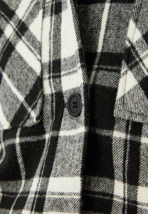 Schwarzes und weißes karierte Flanellstoff mit weicher Textur, versehen mit einem schwarzen Knopfdetail auf der Vorderseite.