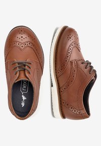 Brązowe skórzane buty z detalami w stylu brogue, z sznurowaniem i białą gumową podeszwą. Posiadają okrągły nos i tłoczone akcenty.