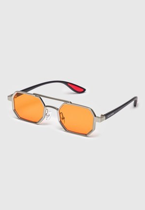 Achthoekige zonnebril met oranje getinte glazen, zilverkleurig metalen montuur, zwarte poten met rode binnenpunten en verstelbare neuspads.