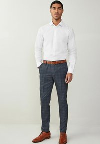Camisa blanca de botones, pantalones a cuadros en azul marino, cinturón de cuero marrón y zapatos de vestir marrones a juego. Diseño elegante con silueta ajustada.