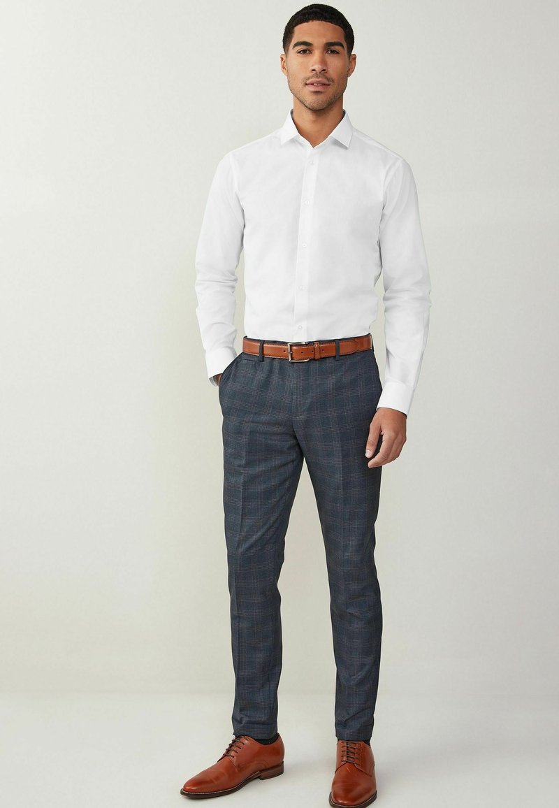 Camisa blanca de botones, pantalones a cuadros en azul marino, cinturón de cuero marrón y zapatos de vestir marrones a juego. Diseño elegante con silueta ajustada.
