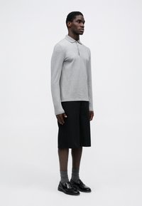 Cămașă polo gri cu mânecă lungă și guler, asortată cu pantaloni scurți negri până la genunchi. Completată cu șosete gri și mocasini negri.