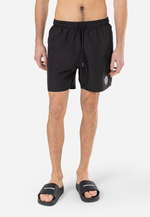 Black swim shorts with an elastic waistband and drawstring, featuring a small logo on the left leg, paired with black slide sandals.