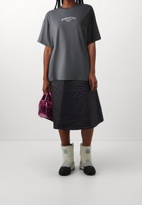 Szara, oversize t-shirt z napisem "MANHATTAN", czarna pikowana spódnica, błyszcząca różowa torebka i białe oraz czarne zimowe buty.