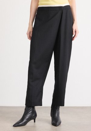 Zwarte op maat gemaakte broek met een losse pasvorm, voorzien van een vlakke voorkant, zijzakken en een gladde textuur. Gecombineerd met puntige zwarte enkellaarzen.