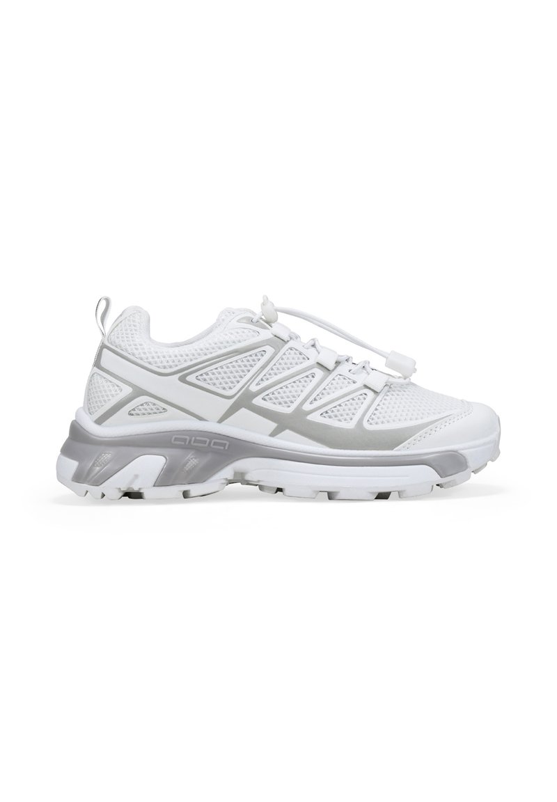 Zapatilla deportiva blanca y gris con parte superior de malla, lengüeta en el talón y cordones elásticos sin nudos con cierre de toggle, mostrada en perfil lateral.