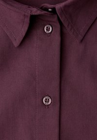 Dunkelviolettes Hemd mit klassischem Kragen, mit Knopfverschluss und Logodetail am Knopf. Hergestellt aus gewebtem Stoff mit etwas strukturierter Oberfläche.