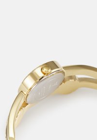 Goldfarbene Armbanduhr mit rundem Gehäuse, strukturiertem Kronenring und glatten Armbändern. Metallmaterial mit reflektierender Oberfläche und minimalistischem Design.