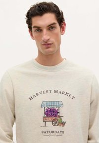 Sudadera gris clara con un gráfico de un carro de frutas con uvas y plantas en macetas, etiquetado "MERCADO DE COSECHA LOS SÁBADOS".