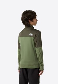 Oliiviroheline pehme kestaga jakk kõrge kraega ja kontrastsete tumeroheliste õlapaneelidega. Tagaküljel logoga. Pikkade varrukatega, tekstureeritud kangas.