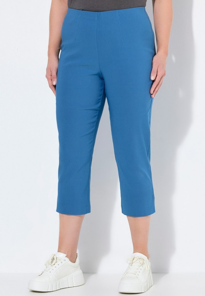 Pantalones cortos azules de tela suave, con corte recto. Combinados con zapatillas blancas, que presentan un diseño limpio y sin patrones visibles.