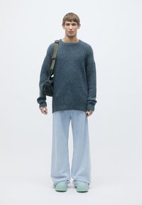 Oversized blue knitted sweater, loose light blue jeans, and green slip-on shoes. Accessories include a black shoulder bag.