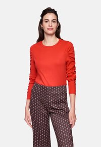 Red long-sleeve shirt with gathered shoulders paired with patterned black and red wide-leg pants featuring diamond shapes.