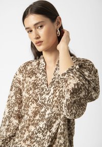 Braun- und cremefarbenes, gemustertes Blusenshirt mit V-Ausschnitt, weiten Ärmeln und leichtem Stoff, der ein texturiertes, abstraktes Design aufweist.