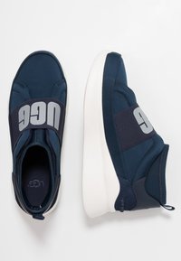 Granatowe buty sportowe z materia�łową cholewką, elastycznym paskiem z logo i białą, amortyzującą podeszwą. Gładka tekstura z przeszyciami.