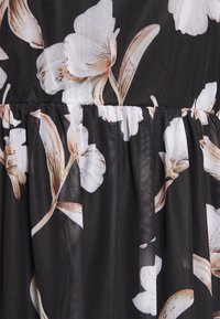 Tissu noir à texture transparente, présentant de grands motifs floraux blancs et beiges. Design évasé avec des détails froncés au niveau de la taille.
