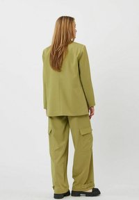 Chaqueta ajustada de color verde oliva con corte recto y pantalones cargo a juego que presentan bolsillos laterales y un ajuste relajado. Tejido texturizado con costuras visibles.
