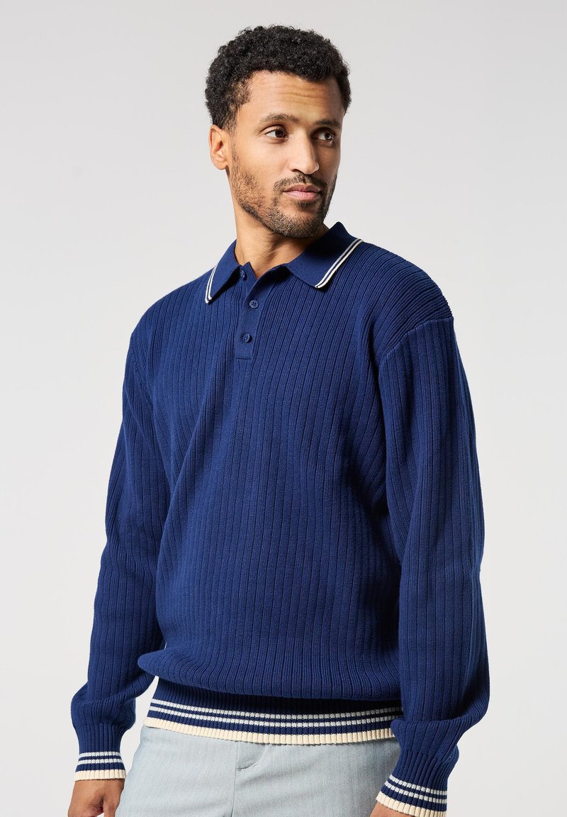 Námořnický pletený polo svetr s dvouknoflíkovou légou, zdobený kontrastním bílým pruhovaným límcem a manžetami. Měkká, strukturovaná tkanina.