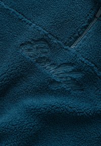 Teal fleece pullover med lynlås, tekstureret overflade og prægede "Brooklyn" logo, der fremhæver varme og komfort.