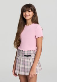 Top corto a maniche corte di un rosa chiaro a costine con orlo scallop, abbinato a una gonna a pieghe in plaid grigia, rosa e bianca, con una cintura nera.