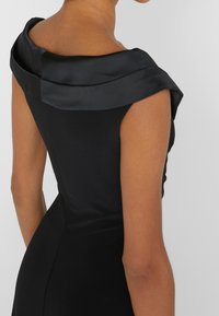 Černé šaty s strukturovaným, skládáním saténového výstřihu. Materiál je hladký a přiléhavý, zvýrazňuje ramena a pas.