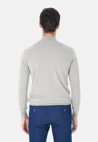Maglione grigio chiaro con un design aderente, maniche lunghe, colletto e polsini a coste, realizzato in materiale morbido. Indossato con jeans blu scuro.