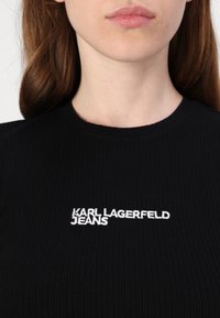 Schwarz gestreiftes T-Shirt mit dem weißen, gestickten Schriftzug "KARL LAGERFELD JEANS" auf der Vorderseite. Klassischer Rundhalsausschnitt.
