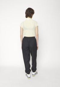 Light yellow, textured, cropped shirt with short sleeves paired with loose-fitting black pants and white sneakers with yellow accents.