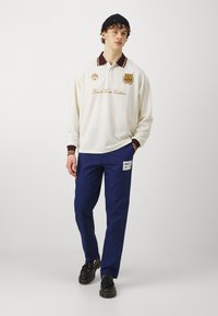 Hvit langermet polo-skjorte med burgunder krage og mansjetter, med brodert logo; parret med marineblå bukser og sorte sko.