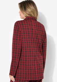 Blazer de cuadros en rojo y negro con solapa, mangas largas, corte estructurado y textura suave. La vista trasera muestra costuras ajustadas.
