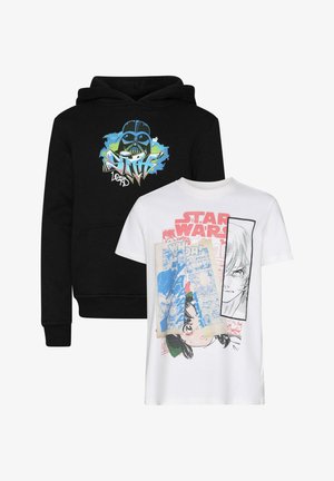 Czarna bluza z kapturem z graficznym wzorem przedstawiającym maskę i kolorowe akcenty, zestawiona z luźnymi niebieskimi spodniami cargo z denimu i białymi tenisówkami.