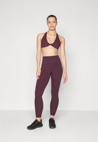 Sportieve tweedelige outfit bestaande uit een diep bordeaux halterbrasserie en hoge taille leggings, beide gemaakt van zacht, gestructureerd materiaal.