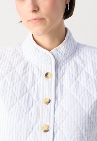Jaqueta acolchoada em riscas azul claro e brancas, com um colarinho alto e quatro botões em tom creme com superfície texturizada.