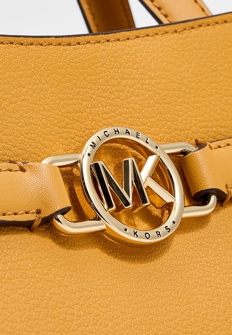 Sac à main en cuir texturé jaune avec un logo en matériel doré de forme circulaire affichant la marque "Michael Kors" et le sigle "MK".