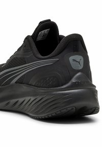 Zapatilla deportiva negra con parte superior de tela texturizada, suela de goma lisa y sutiles acentos grises con logo en el talón.
