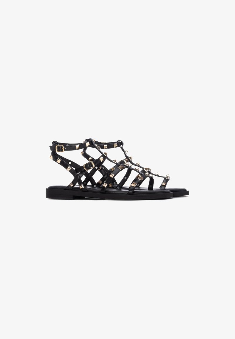 Zwarte leren sandalen met een bandjesontwerp, voorzien van gouden studs en gespen, platte zool en open teen voor ventilatie.