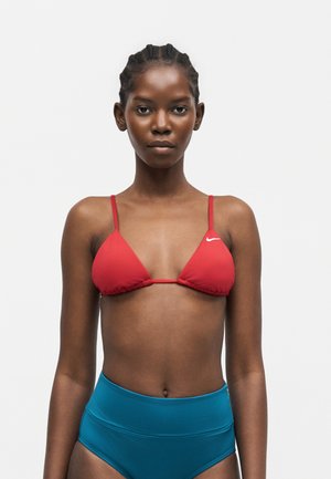 Femme aux cheveux tressés portant un haut de bikini rouge Nike et un bas de bikini bleu taille haute sur un fond blanc uni.