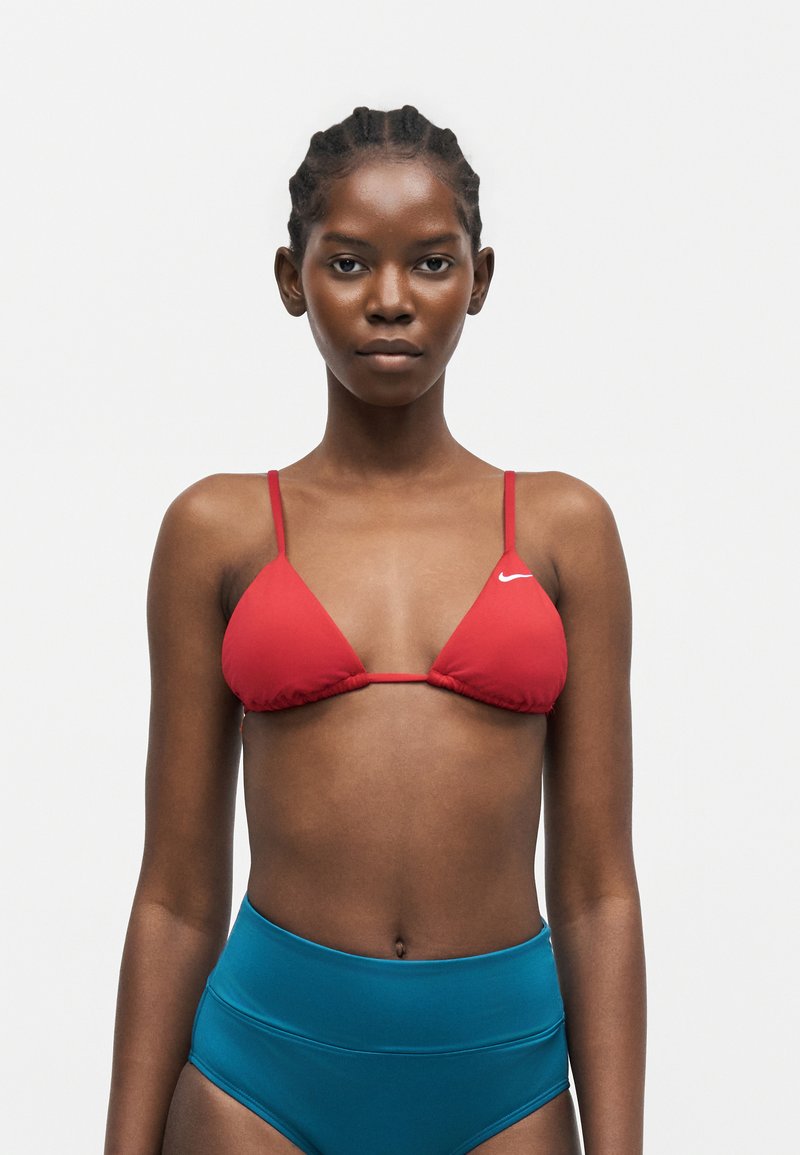 Γυναίκα με πλεγμένα μαλλιά φοράει κόκκινο τοπ μαγιό Nike και μπλε ψηλόμεσα κάτω μέρη μαγιό σε λευκό φόντο.