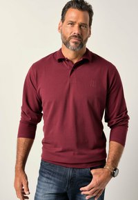 Polo a maniche lunghe color bordeaux con colletto, dotato di un piccolo logo in rilievo sul petto e polsini a coste, abbinato a jeans scuri.