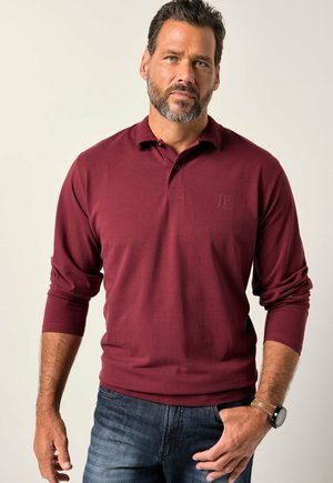 Burgunderfarbendes Langarm-Polo-Shirt mit Kragen, versehen mit einem kleinen, geprägten Logo auf der Brust und gerippten Bündchen, kombiniert mit dunklen Jeans.
