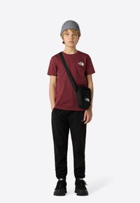 Karamelrød T-shirt med logo, sorte bukser og robuste sorte sko. Grå strikket hue og en lille sort crossbody-taske tilføjede detaljer.