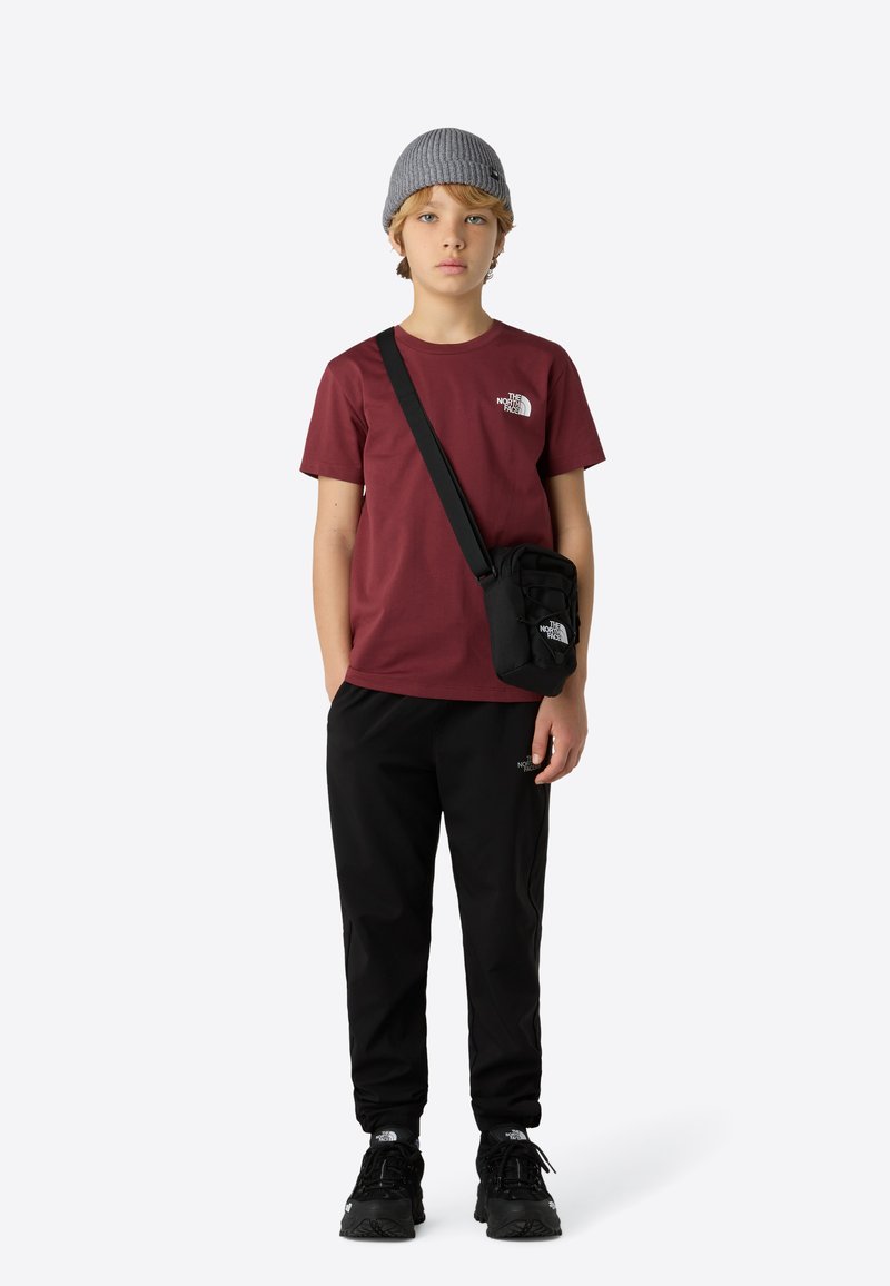 Karamelrød T-shirt med logo, sorte bukser og robuste sorte sko. Grå strikket hue og en lille sort crossbody-taske tilføjede detaljer.
