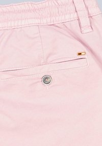 Light pink shorts with an elastic waistband, featuring a rear pocket with a button and a small orange accent near the pocket seam.