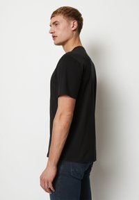 Camiseta de algodón negra con mangas cortas y cuello redondo, exhibida en un modelo visto de lado, con una forma ajustada.