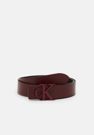 Ceinture en cuir bordeaux foncé enroulée avec une boucle logo "CK" assortie et un marquage en relief subtil sur la sangle sur fond blanc.
