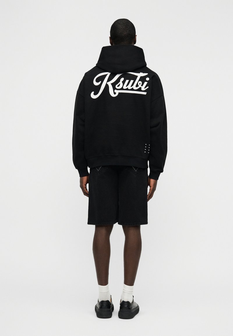 Μαύρο φούτερ με κουκούλα με λευκό λογότυπο "Ksubi" στην πλάτη, συνδυασμένο με μαύρο σορτς. Διαθέτει άνετη εφαρμογή και υφασμάτινη υφή. Μαύρα αθλητικά παπούτσια και λευκές κάλτσες.