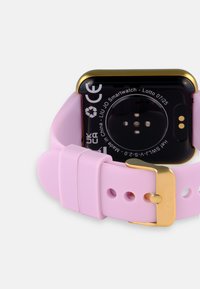 Reloj inteligente con esfera negra y acentos dorados; cuenta con una suave correa de silicona rosa claro con una hebilla plateada y agujeros para ajuste.