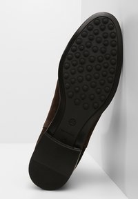 Semelle en daim brun avec une surface texturée et adhérente comportant des motifs circulaires ; conçue pour la traction et la durabilité. Taille 37 en relief.